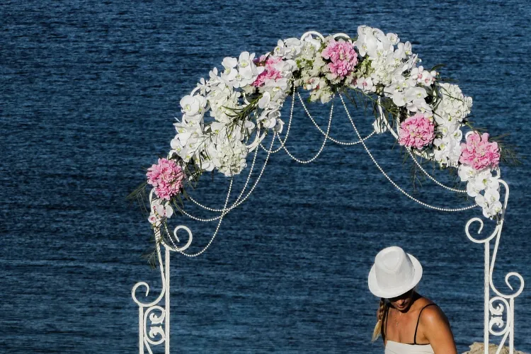 A beach wedding arch, made of white metal and embellished with white and pink flowers.