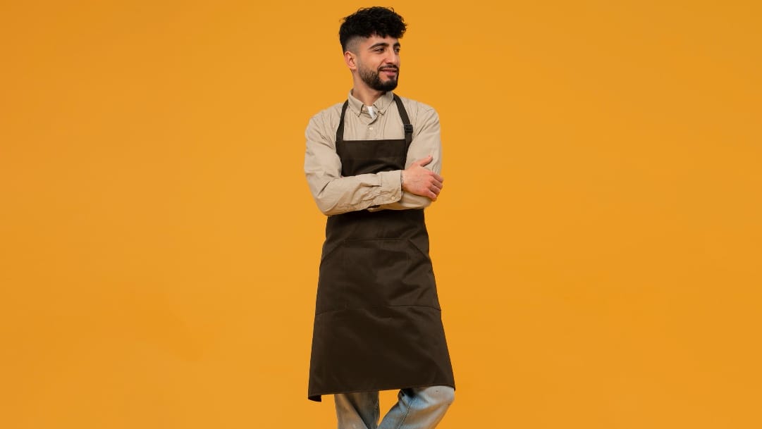 A man in a black apron standing against a yellow background.