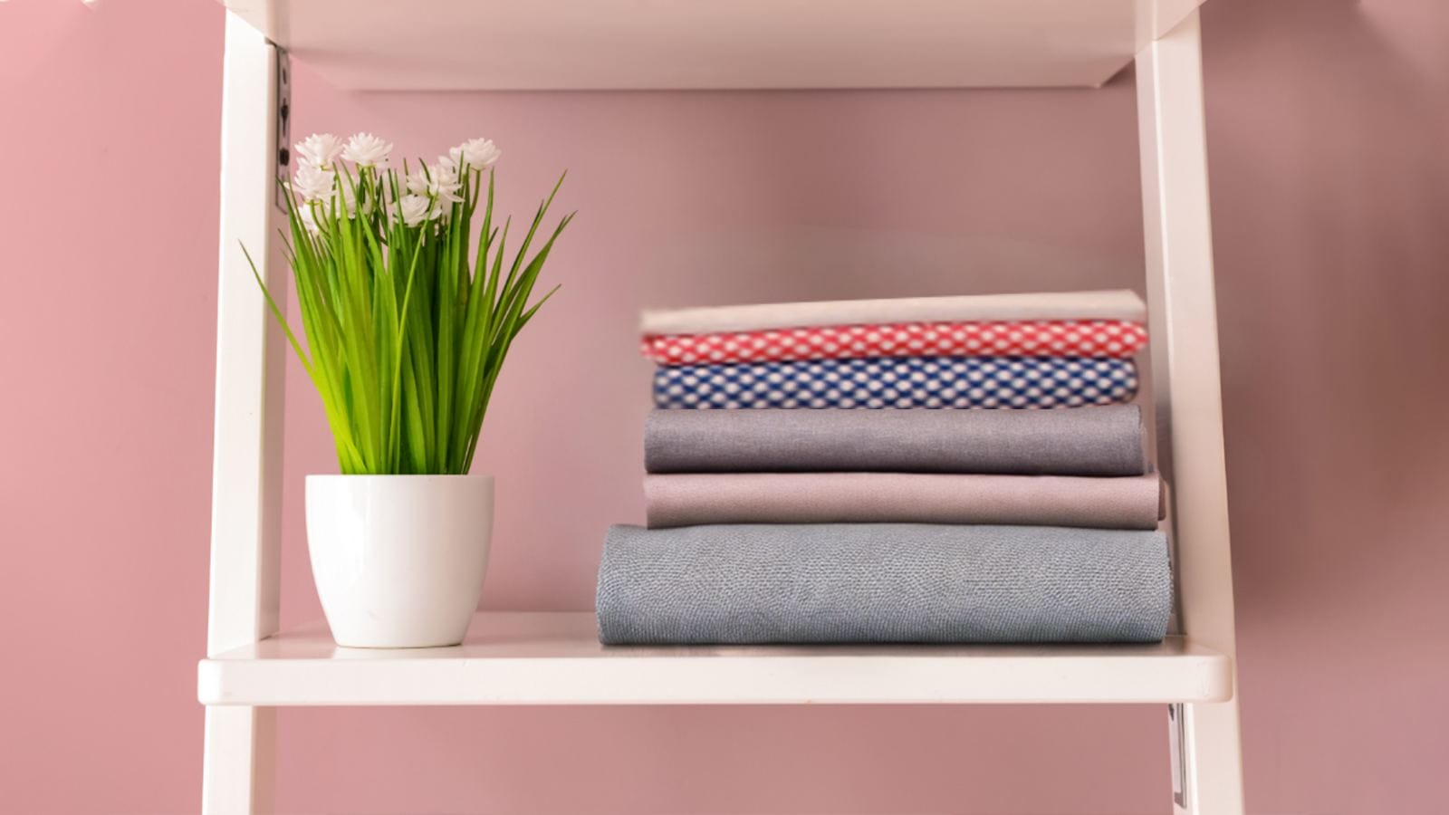A stack of fabrics on a white ladder against a pink wall.