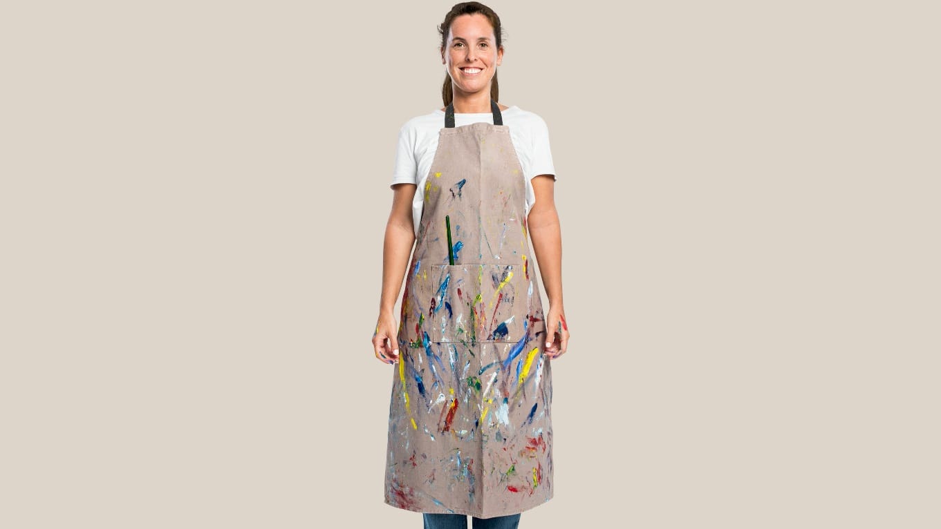 A woman wearing an apron with paint splatters on it.
