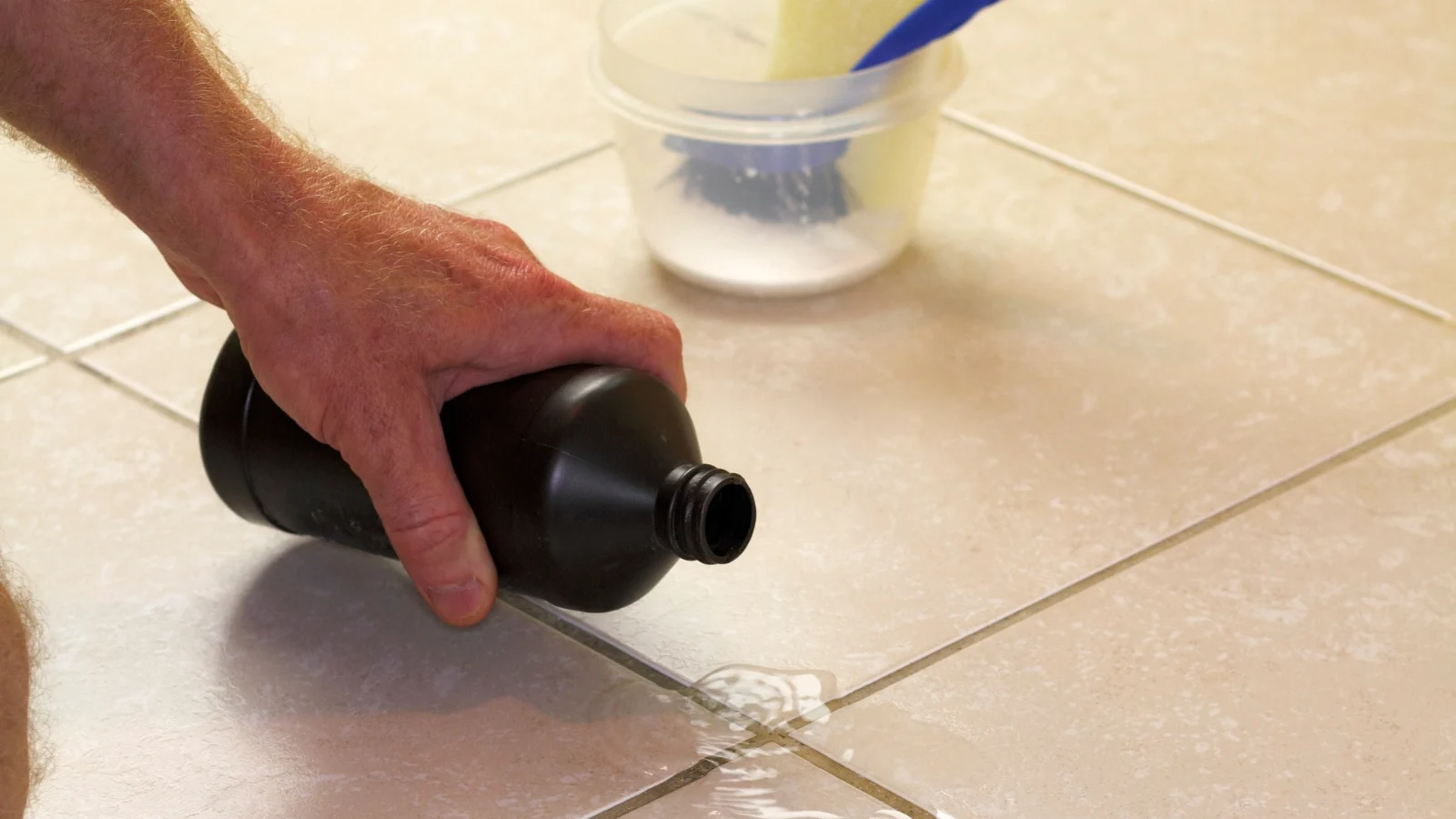 A person cleaning a tile floor with a bottle.