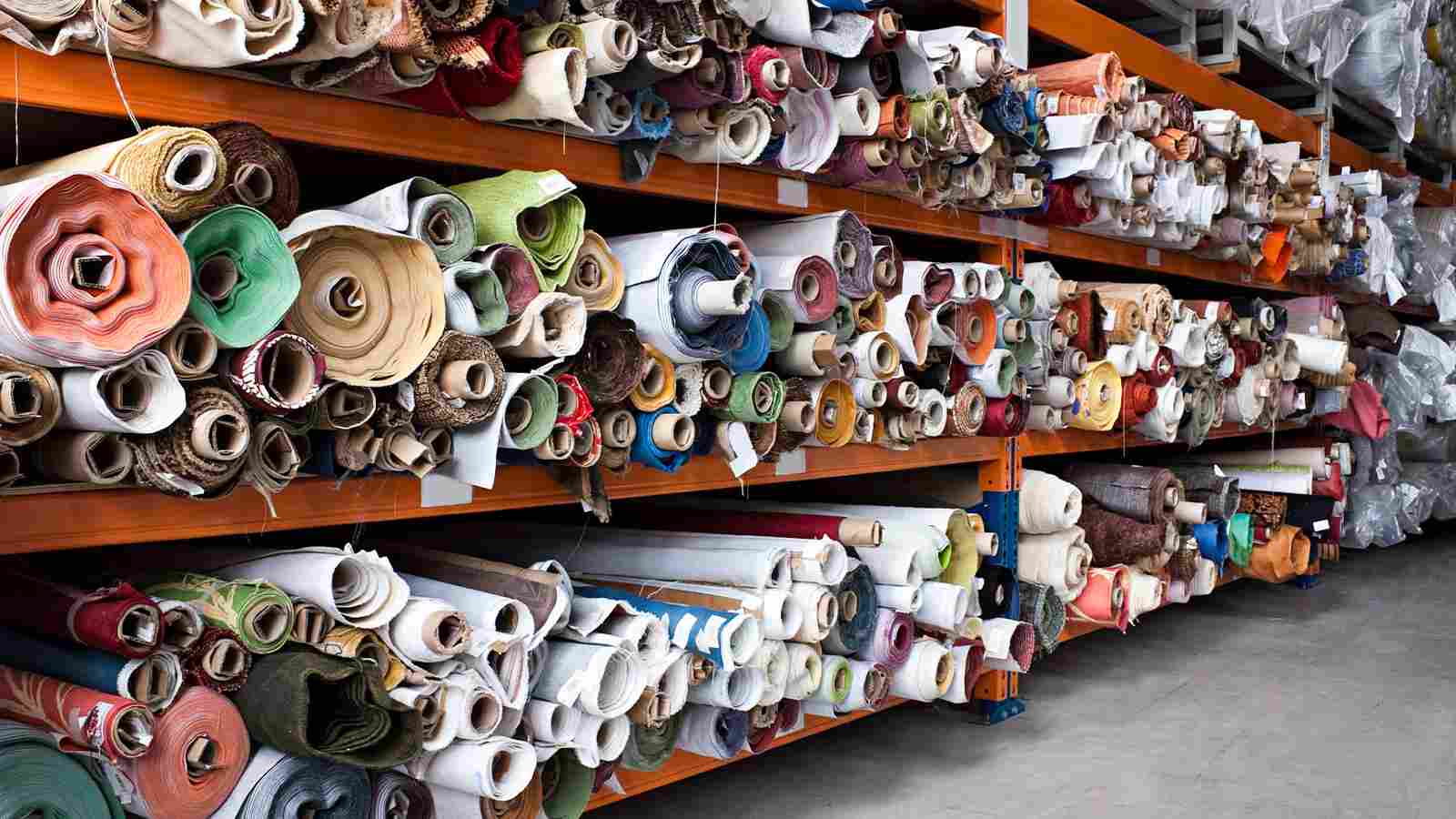 Many rolls of fabric are on shelves in a warehouse.
