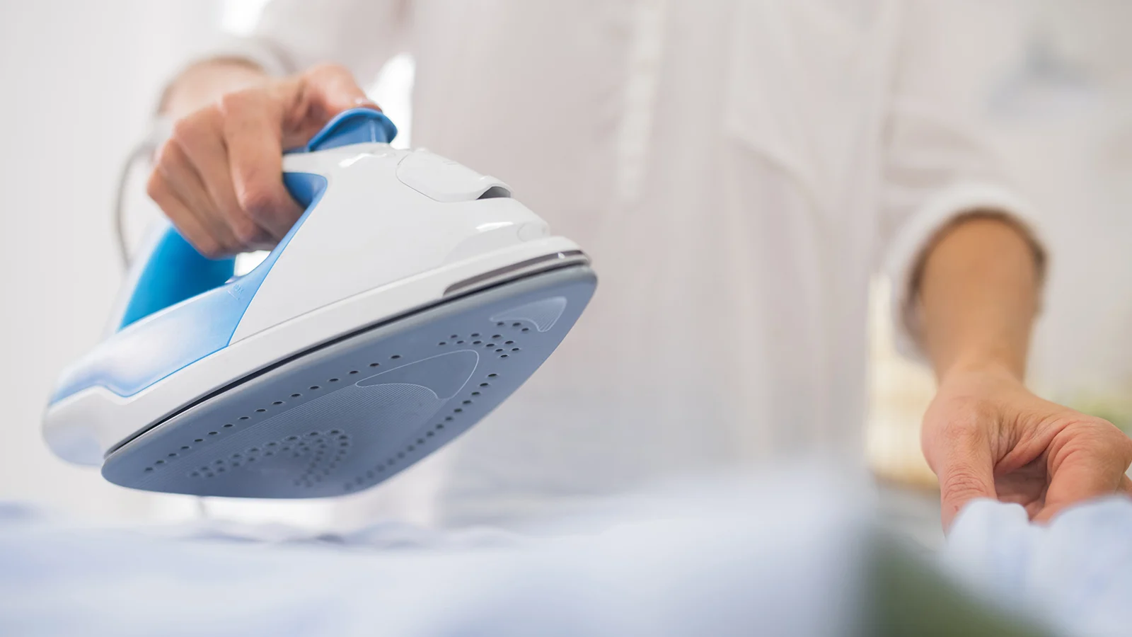 A woman is ironing a shirt with a blue and white iron.