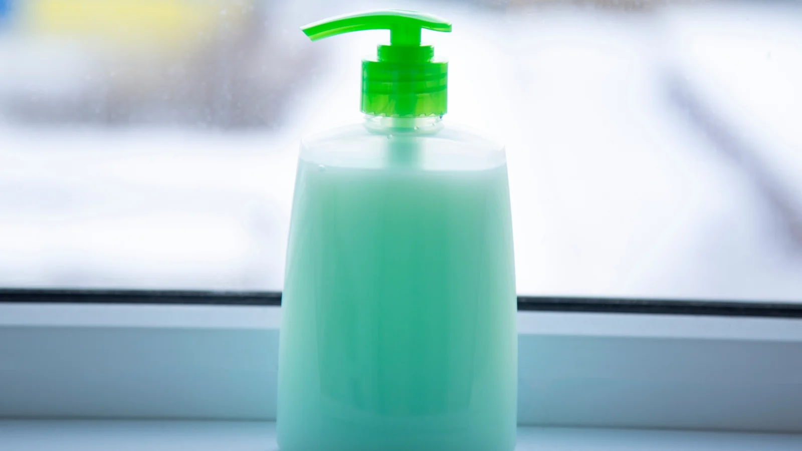 A bottle of green soap sitting on a window sill.