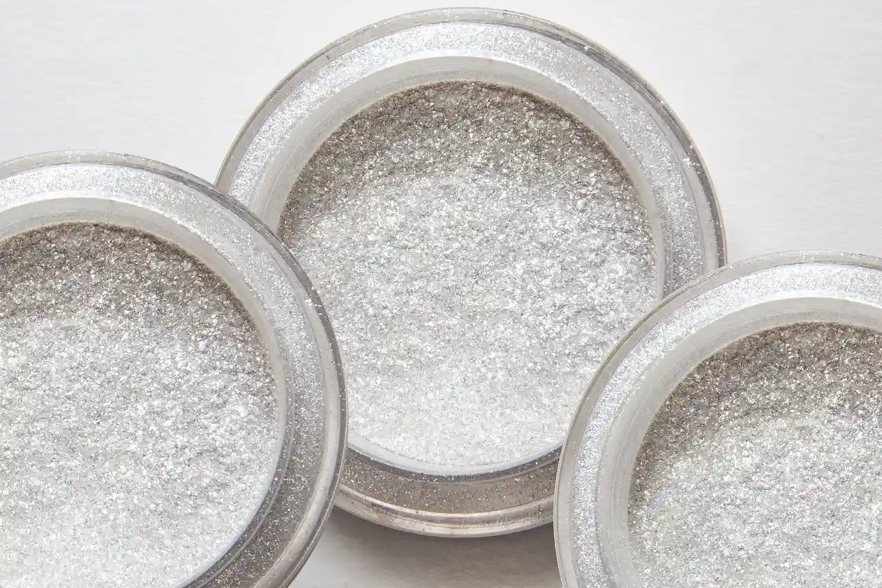 Three silver glitter powderon a white surface.